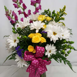 Bouquet of white daisies, yellow roses, and purple snapdragons in a glass vase