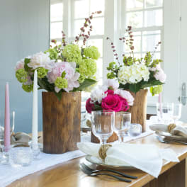 Floral table centerpieces with pink, white, and green blooms in wooden vases