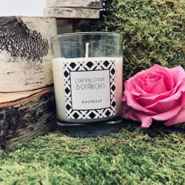 Pink rose beside a labeled glass candle on moss and wood