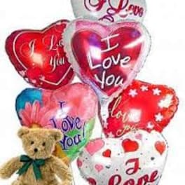 Cluster of heart-shaped I Love You balloons with a small tan teddy bear with green ribbon