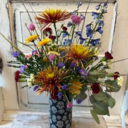 Mixed bouquet in a skull-patterned vase with spiky orange blooms and blue flowers