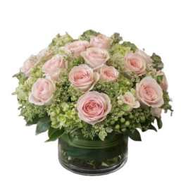 Pink roses arranged in a low glass vase with green hydrangeas