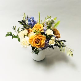 Mixed bouquet of orange, white, and blue flowers in a white vase