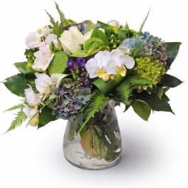 Mixed bouquet of white orchids, hydrangeas, and roses in a glass vase