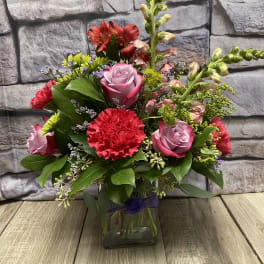 Mixed bouquet of roses, carnations, and snapdragons in a glass vase