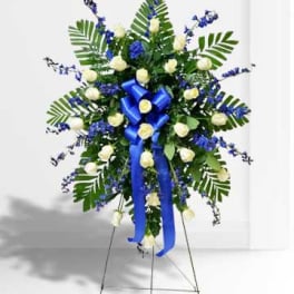 Standing floral spray with white roses, blue flowers, and a blue ribbon