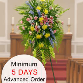 Tall standing funeral spray of pink, yellow, and blue flowers on an easel in a church aisle