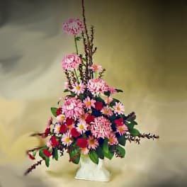 Tall pink and red mixed flower arrangement in a white vase