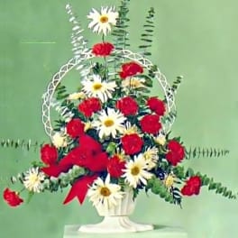 Tall red carnation and white daisy arrangement in a white urn with a red bow.