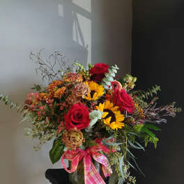 Bouquet of red roses and sunflowers in a glass vase with a pink ribbon