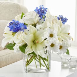 White lilies, roses, and daisies with blue flowers in a glass vase