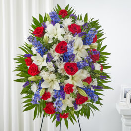 Large standing floral spray with red roses, white lilies, and blue flowers