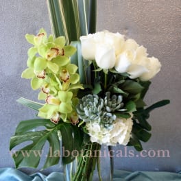 White roses and green orchids in a glass vase with tropical leaves