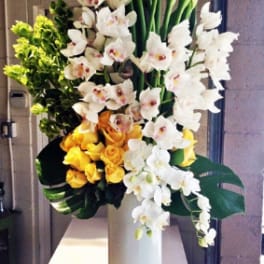Tall floral arrangement with white calla lilies, orchids, and yellow roses in a white vase