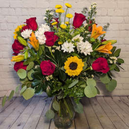 Mixed bouquet of red roses, lilies, white daisies, and a sunflower in a glass vase