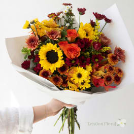Handheld bouquet of sunflowers, roses, and chrysanthemums wrapped in white paper