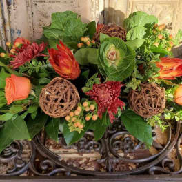 Low floral arrangement with orange roses and red blooms in a decorative container