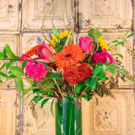 Bright mixed bouquet in a tall glass vase with pink, orange, and yellow blooms