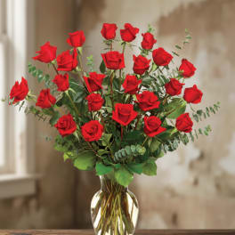 Tall arrangement of long-stem red roses in a clear glass vase on a wooden table