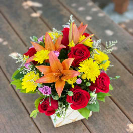 Bouquet of red roses, orange lilies, and yellow daisies in a square box