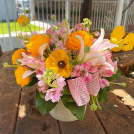 Bouquet of orange and pink flowers in a white vase with a pink ribbon