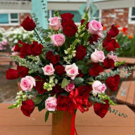 Red and pink roses arranged in a tall vase with ribbon