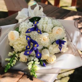 Bouquet of white flowers with cream roses and blue irises in pale wrapping