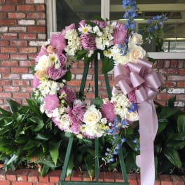 Floral wreath on an easel with pink, white, and blue flowers and a lavender ribbon
