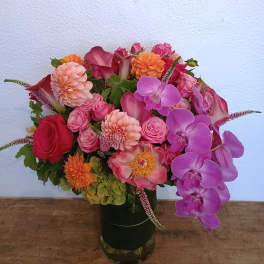Colorful bouquet of roses, dahlias, calla lilies, and orchids in a glass vase
