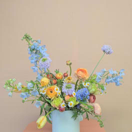 Pastel mixed bouquet in a light blue vase with blue and yellow blooms