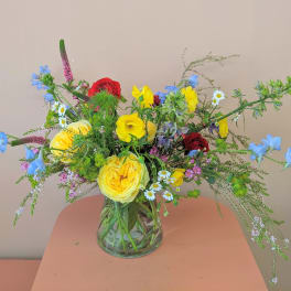 Mixed bouquet of yellow, red, and blue flowers in a clear glass vase
