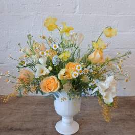 Yellow and peach floral arrangement in a white pedestal vase