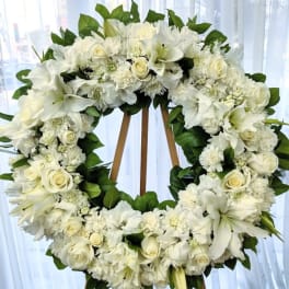 White floral wreath on a wooden easel with roses and lilies