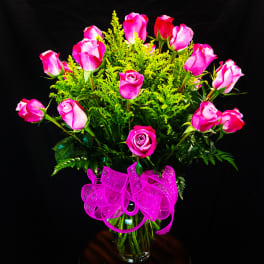 Pink roses in a glass vase with a bright pink ribbon