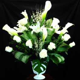 White calla lilies and roses in a white vase with large green leaves