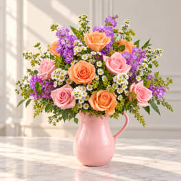 Pink and peach roses with purple flowers in a pink pitcher vase