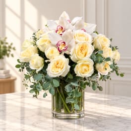 White roses and orchids arranged in a clear glass vase