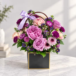 Pink and purple flower arrangement in a black square box with a lavender ribbon