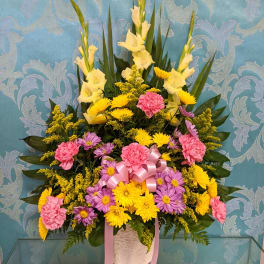 Tall floral arrangement with yellow, pink, and purple blooms in a white vase