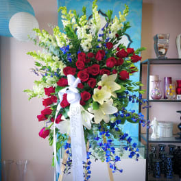 Tall floral arrangement with red roses, white lilies, and blue flowers on an easel