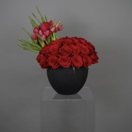 Red roses and pink tulips arranged in a black vase
