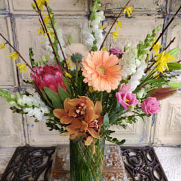 Mixed bouquet in a clear glass vase with pink, peach, white, and yellow blooms