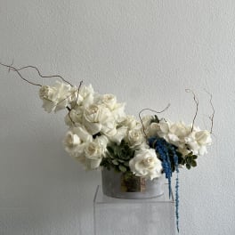 White rose arrangement with blue hanging accents in a gray container
