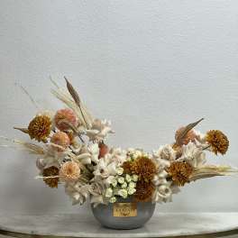 Low floral arrangement in a gray vase with cream and peach blooms