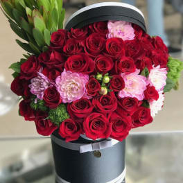 Red roses and pink flowers arranged in a black hat box