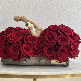 Red roses arranged in a rustic wooden container with a branch accent