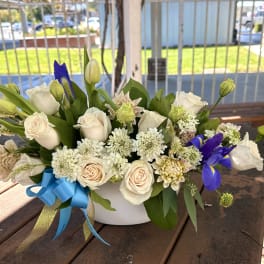 White and cream flower arrangement with blue irises in a white bowl vase