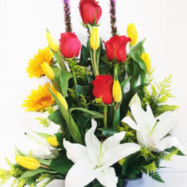 Tall mixed arrangement of white lilies, red roses, yellow tulips and sunflowers in a low black container