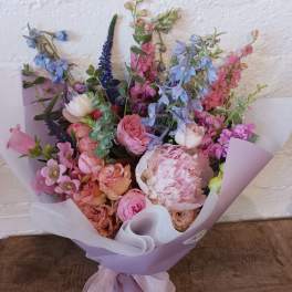 Pastel bouquet of pink, blue, and peach flowers wrapped in lavender paper
