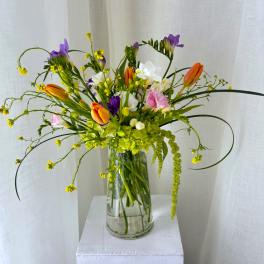 Mixed bouquet of orange tulips, purple freesia, and white blooms in a glass vase